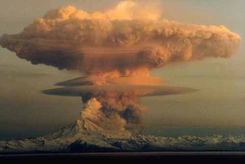 Ascending eruption cloud from the Mount Redoubt volcano in 1990 as viewed to the west from the Kenai Peninsula. The mushroom-shaped plume rose from avalanches of hot debris that cascaded down the north flank of the volcano. A smaller, white steam plume rises from the summit crater. (Photo by R. Clucas)