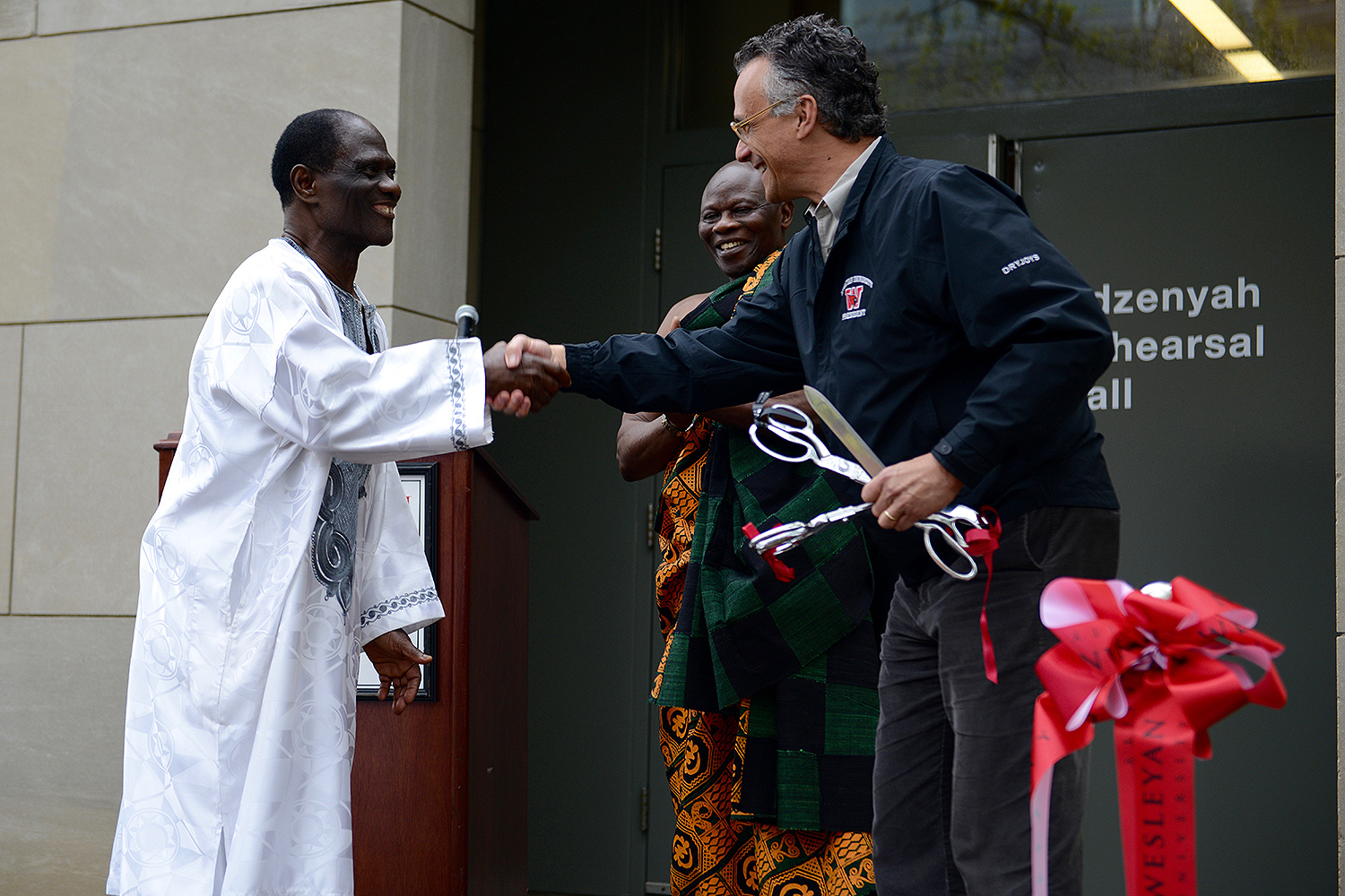 Wesleyan President Michael Roth, at right, congratulates Abraham Adzenyah for teaching at Wesleyan 46 years and for the naming of the Abraham Adzenyah Rehearsal Hall (formerly the Center for the Arts Rehearsal Hall). A ribbon cutting ceremony took place May 7. 