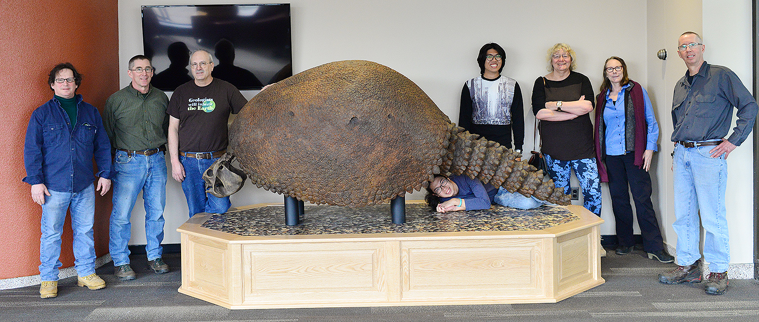 he Glyptodon, a giant fossil cast that has been in storage since 1957, is now on display in Exley Science Center. Several members of the Wesleyan community helped install the 8-foot-long cast on Feb. 26. Pictured, from left, are Joel LaBella, facility manager for the Earth and Environmental Sciences Department; Bruce Strickland, Instrument maker specialist; Jim Zareski, research assistant/lab manager for the Earth and Environmental Sciences Department; Freeman Scholar Yu Kai Tan ’20; Freeman Scholar Andy Tan ’21; Ellen Thomas, the Harold T. Stearns Professor of Integrative Sciences; Annie Burke, chair and professor of biology; and David Strickland, instrument maker. Glyptodon means “grooved or carved tooth” in Greek. The creature lived approximately 2 million to 10,000 years ago.