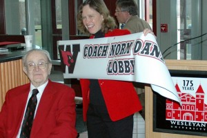 Barbara-Jan Wilson, vice president for University Relations, holds up a banner declaring the space "Coach Norm Daniels Lobby" during Daniels's 100th birthday celebration. 