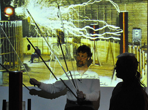 Vacek Miglus, lab technician and curator of the Physics Department, shows the students how various lamps are lit by a Tesla coil without being attached to wires. Brian Stewart is on the right. 