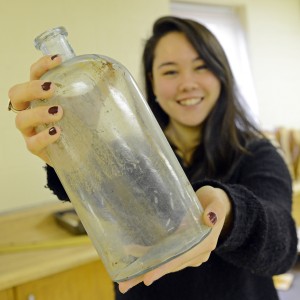 Amy Cao '15 holds a large glass bottle discovered during the Beman excavation.  The bottle, which will be on display in the “Unearthing Community" exhibit, was manufactured by a company called Whittal, Tatum & Company that specialized in glassware for druggists and chemists.