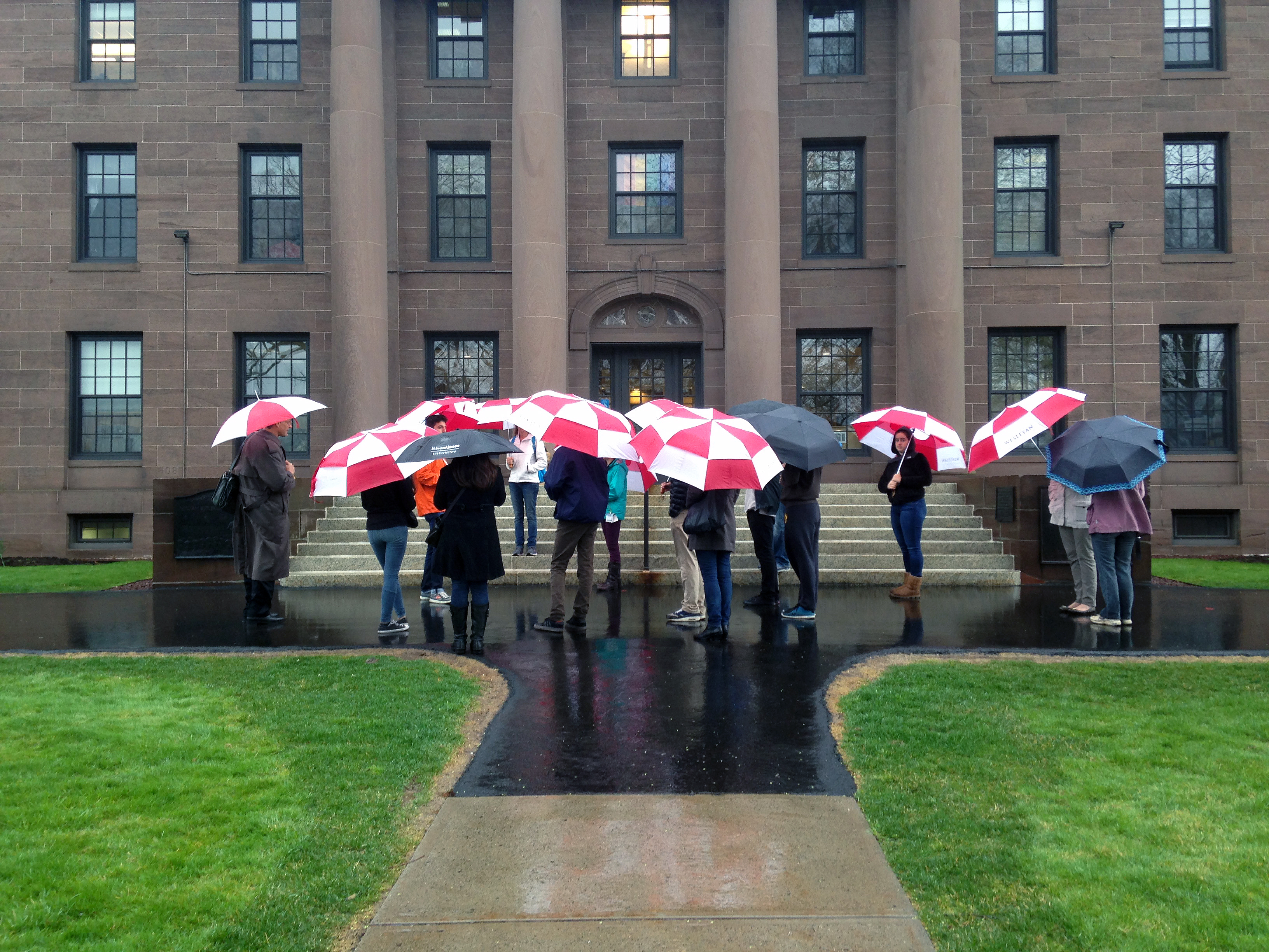 In a moment of serendipity, Wesleyan President Michael Roth found his walk to work coinciding with the path of an Admission tour group. With his red umbrella aloft, he walked into the crowd of prospective parents and students near the steps of North College. He listened for a while before blowing his cover by asking “Does anyone have any questions for the president this morning?”   Members of the group captured the moment on their smartphones. 