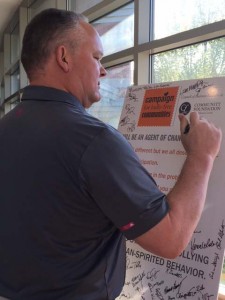 Mike Whalen stands in front of a poster and signs in.