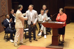 Jed D. Hoyer ’96 stands on stage and president Roth shakes his hand while Daphne Kwok ’84 looks on.