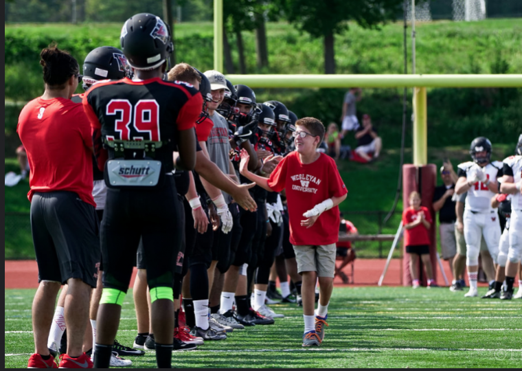 Michael receives high-fives and handshakes from the Wesleyan football team. 